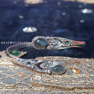 Pode incluir: Pulseira de bracelete de prata com duas pedras azul-esverdeadas iridescentes engastadas em engastes de prata ornamentados. A pulseira é aberta e flexível.