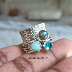 以下が含まれることがあります： テクスチャ加工されたバンドと3つの宝石が付いたシルバーリング。宝石はライトブルー、ダークブルー、ブラウンです。