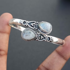 Op de afbeelding: Een zilveren armband met twee druppelvormige maansteen edelstenen. De armband heeft een ingewikkeld ontwerp met zilveren filigraan.