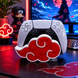 Könnte beinhalten: Ein weiß-schwarzer Videospiel-Controller auf einem Ständer in Form einer roten Wolke mit weißem Rand. Der Ständer hat eine strukturierte Oberfläche und steht vor einem Computermonitor, der eine Figur in einem roten Wolkenumhang zeigt.