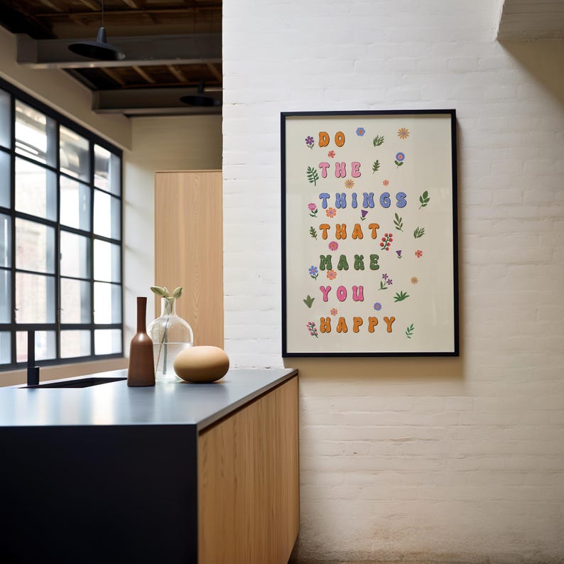 May include: A framed print with a white background and black frame. The print features the text "Do the things that make you happy" in colorful, stylized letters with small floral illustrations scattered throughout.