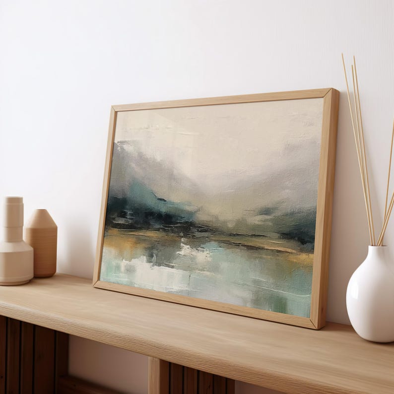 May include: A framed abstract landscape painting with muted tones of blue, green, and brown. The painting depicts a hazy, atmospheric scene with a body of water in the foreground and hills in the background.