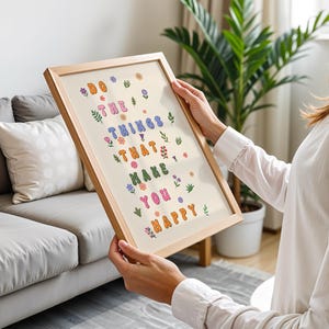 May include: A framed print with a light background and colorful text that reads "Do the things that make you happy". The text is surrounded by small floral illustrations in various colors.