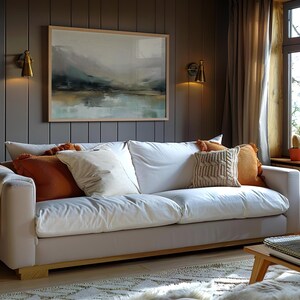 May include: A white sofa with a throw blanket and several pillows in a living room with a window and a painting on the wall.