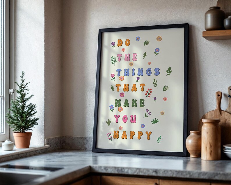 May include: A framed print with a white background and colorful text that reads "Do the things that make you happy". The text is surrounded by small floral illustrations in various colors.