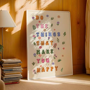May include: A white framed poster with the text "Do the things that make you happy" in colorful, bubble-like letters. The poster is decorated with small, colorful flowers and leaves.