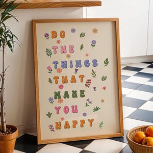 May include: A framed print with a light beige background and the text "DO THE THINGS THAT MAKE YOU HAPPY" in colorful, stylized letters. The letters are surrounded by small, colorful flowers and leaves.