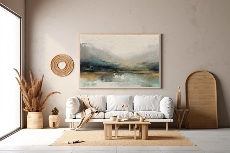 May include: A white sofa with a throw blanket sits in a living room with a large abstract landscape painting on the wall. The painting features shades of blue, green, and brown. The room is decorated in a minimalist style with a wooden floor and a woven rug.