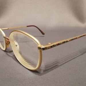 Peut inclure: Lunettes de vue dorées avec des verres transparents et une branche à motifs marrons et multicolores.
