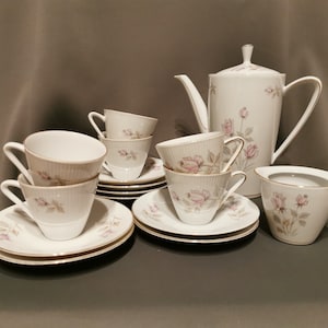 May include: A white porcelain tea set with a floral design. The set includes a teapot, creamer, and four cups and saucers.