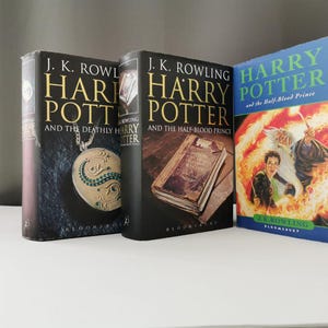 Può includere: Tre libri in brossura rigida in fila, tutti parte della serie di Harry Potter. Il primo libro è "Harry Potter e i Doni della Morte", il secondo è "Harry Potter e il Principe Mezzosangue", e il terzo è "Harry Potter e il Principe Mezzosangue".
