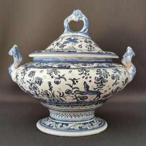 Peut inclure: Un plat de service en céramique blanche avec un motif floral bleu et blanc. Le plat a un couvercle avec une poignée et deux poignées sur les côtés. Le plat est décoré d'un motif floral bleu et blanc et d'un petit oiseau bleu.