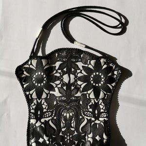 May include: A black and white patterned bag with a black strap. The bag has a floral design with a scalloped edge.