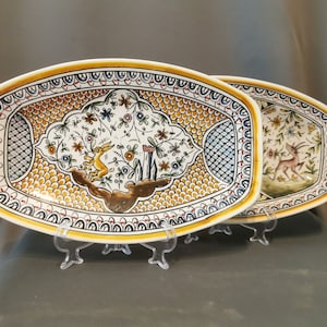 Può includere: Due piatti da portata ovali in ceramica con intricati disegni floreali. Un piatto presenta un coniglio e l'altro un cervo. Entrambi i piatti hanno una gamma di colori giallo, arancione e blu.