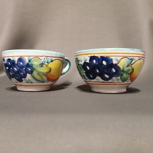 Pode incluir: Duas tigelas de cer&acirc;mica branca com um desenho de frutas azul, verde e amarelo. As tigelas s&atilde;o decoradas com uvas, folhas e uma p&ecirc;ra.