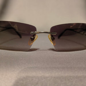 Puede incluir: Un par de gafas de sol plateadas con lentes grises oscuros y detalles amarillos en las patillas.