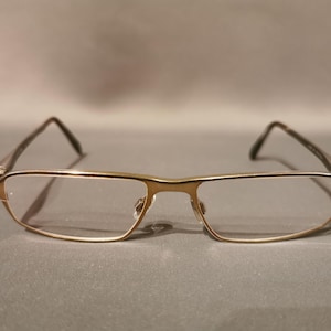 May include: Gold-tone metal eyeglasses with a rectangular frame and clear lenses.