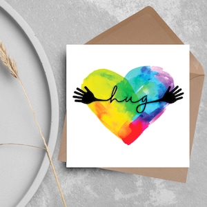Puede incluir: Una tarjeta de felicitación con un corazón de acuarela arcoíris y la palabra "hug" escrita en cursiva negra. Dos manos negras están dibujadas a cada lado del corazón, formando un abrazo.
