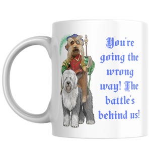 May include: A white ceramic mug featuring a colourful illustration of a shaggy dog with a smaller dog wearing a hat, eyepatch, and green sleeves riding on its back while holding a staff. The text reads, You're going the wrong way! The battle's behind us!