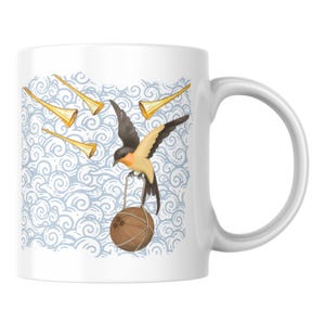 May include: A white ceramic mug featuring a graphic illustration of a swallow bird in flight, carrying a brown coconut tied with string. The background displays a light blue pattern of swirling clouds and three golden trumpet-like shapes.