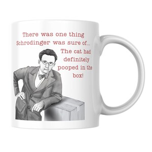 May include: A white ceramic mug featuring a black and white illustration of a man in a suit and bowtie leaning on a box. The red text reads: There was one thing Schrodinger was sure of... The cat had definitely pooped in the box!