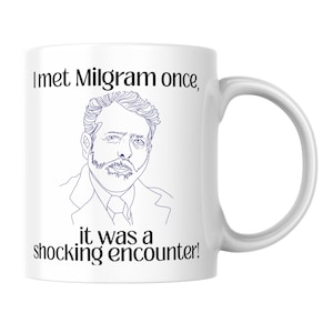 May include: A white ceramic mug featuring a dark blue line drawing of a man with a beard and the black text "I met Milgram once, it was a shocking encounter!" printed above and below the illustration. The mug has a curved handle on the right side.