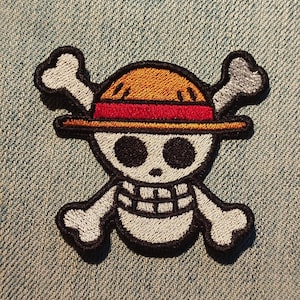 Può includere: Toppa ricamata raffigurante un teschio con cappello di paglia e ossa incrociate. La toppa ha un contorno nero e una fascia rossa sul cappello, su sfondo denim. Il design è un popolare simbolo anime.