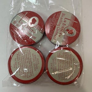 May include: Four vintage La Dainty Bleaching Ointment tins. The round tins have red and silver labels with text and a silhouette. The text includes "Bleaching Ointment" and "Tyson & Co. Inc."