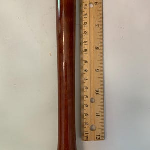 May include: A brown wooden recorder with a ruler next to it. The recorder is approximately 12 inches long. The ruler shows measurements in inches and millimeters.