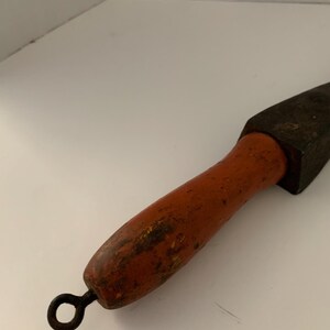 May include: A vintage sharpening steel with a wooden handle and a metal ring at the end. The handle is painted orange and has a worn, distressed look.