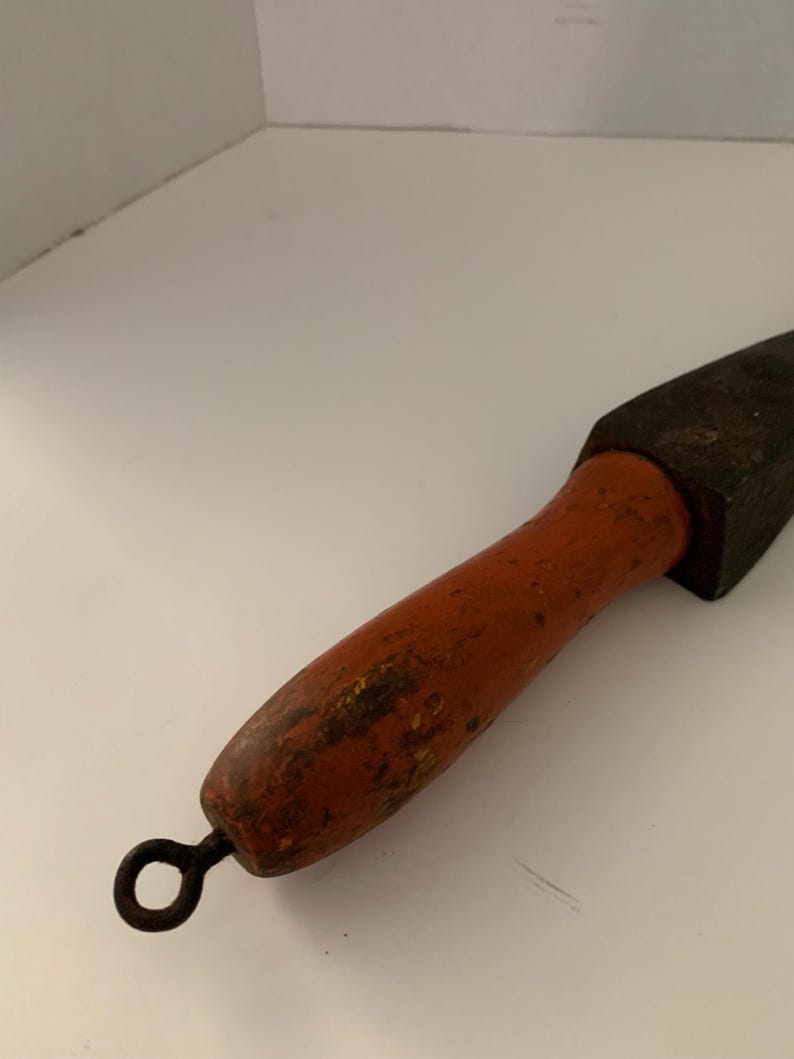 May include: A vintage sharpening steel with a wooden handle and a metal ring at the end. The handle is painted orange and has a worn, distressed look.