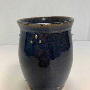 May include: A dark blue ceramic utensil holder with a brown rim and gold speckles.