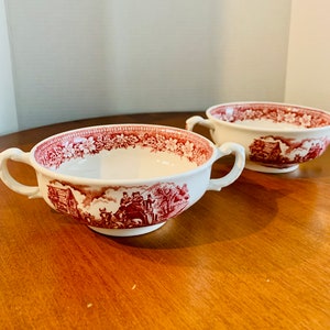May include: Two white ceramic soup bowls with red floral and countryside scene designs. The bowls have two handles.