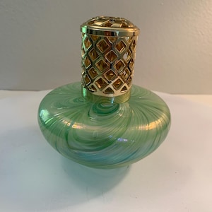 May include: A decorative glass oil lamp with a green and blue swirl pattern. The lamp has a gold-colored metal top with a diamond-shaped lattice design. The lamp is a stylish home decor item.