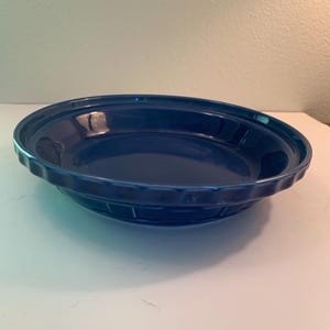 May include: A deep blue ceramic pie dish with a fluted edge. The dish has a glossy finish and a slightly raised base. The pie dish is designed for baking and serving pies.