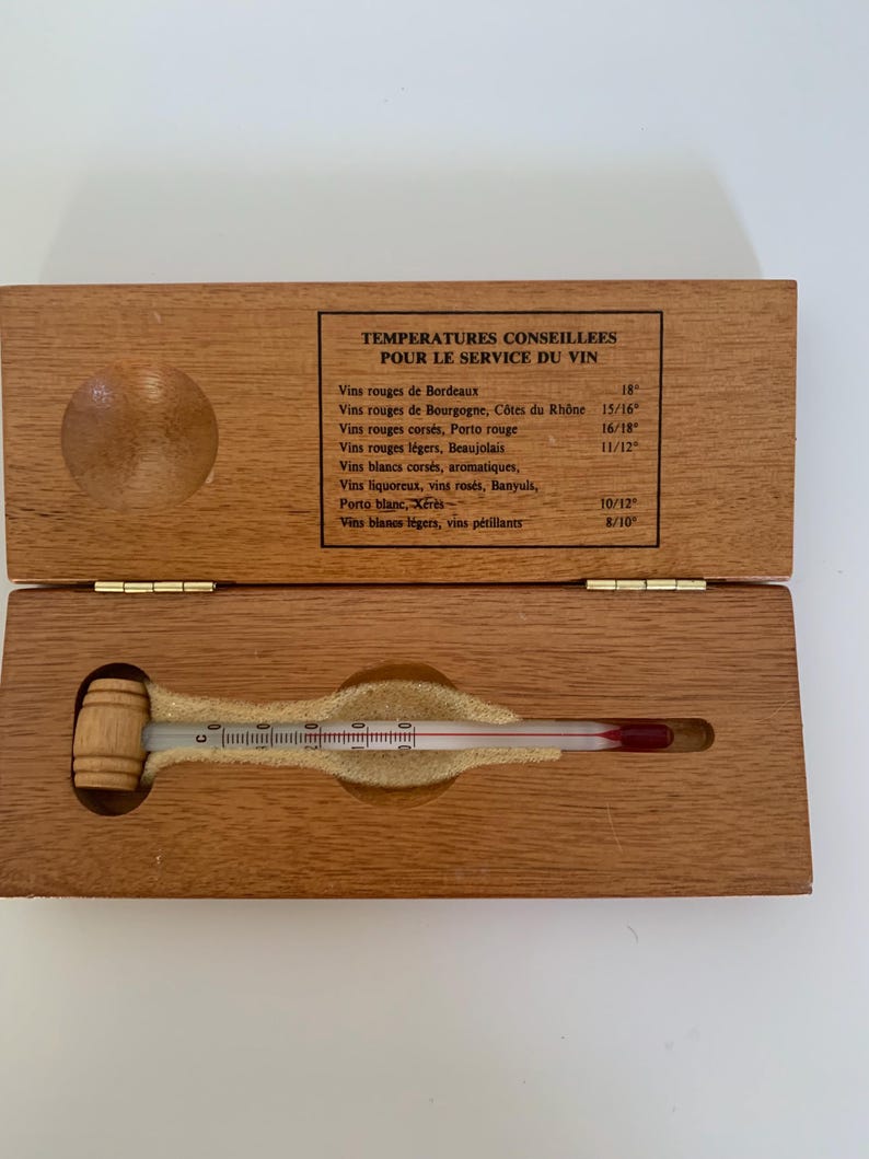 May include: A wooden box with a thermometer inside. The thermometer has a wooden handle shaped like a barrel. The box has a label that reads "Temperatures Conseillees Pour Le Service Du Vin" and lists different types of wine and their recommended serving temperatures in degrees Celsius.