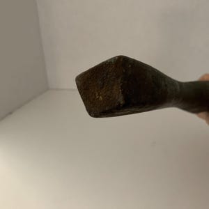 May include: Close-up of the end of a rusty metal tool with a square head.