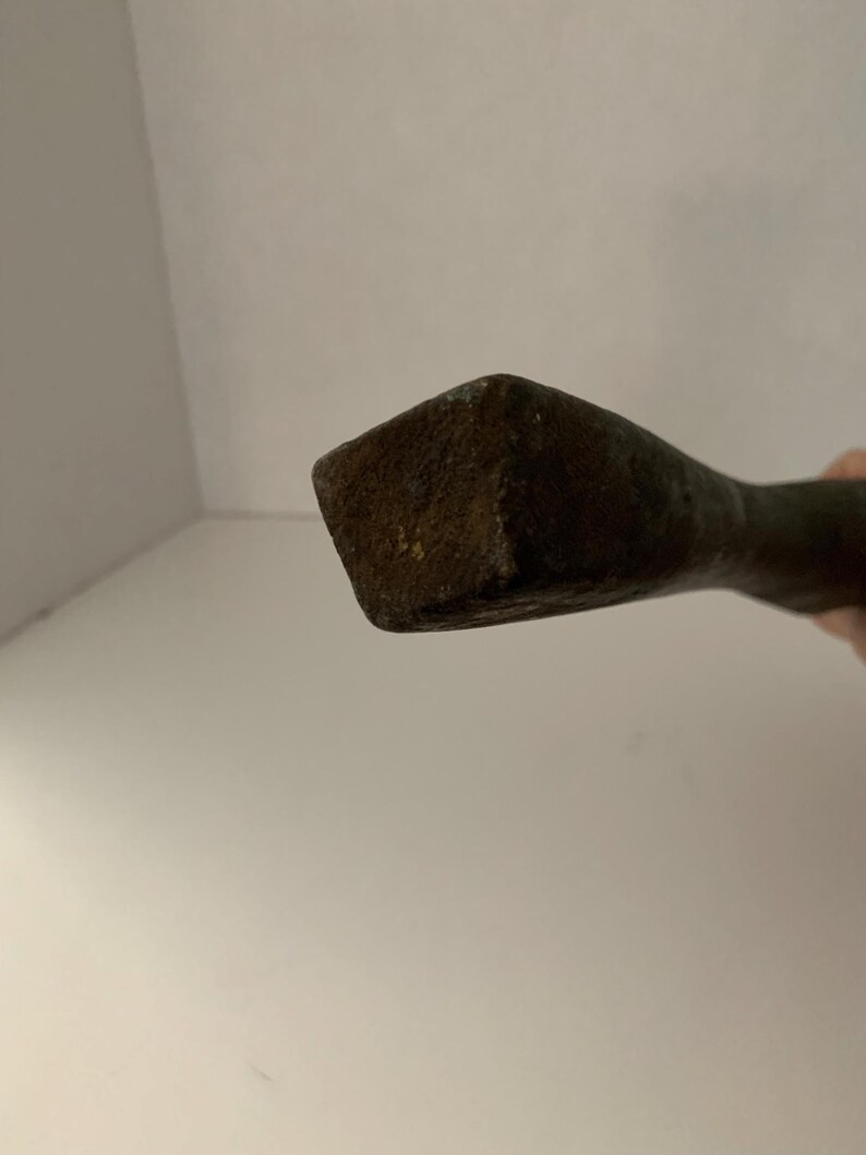 May include: Close-up of the end of a rusty metal tool with a square head.