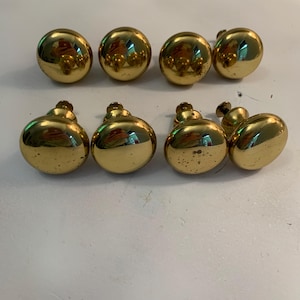 May include: A set of eight round, polished brass cabinet knobs arranged in two rows. Each knob features a smooth, spherical head with a reflective gold-toned finish and a short, cylindrical mounting post extending from the back for attachment.