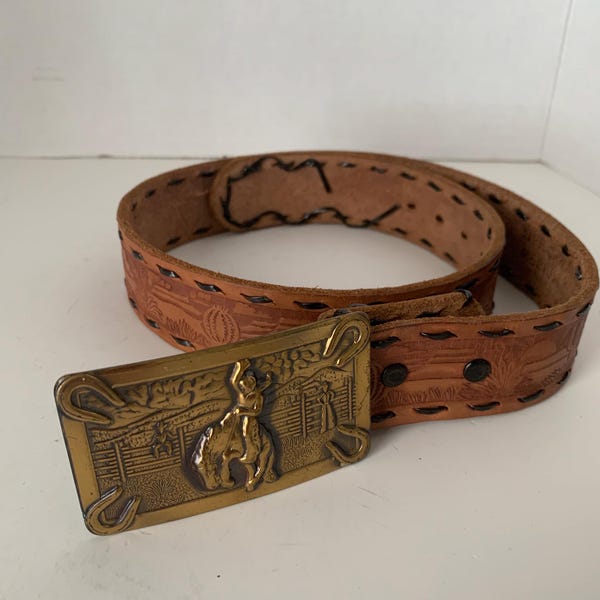 Cinturón vintage de cuero estilo western, de tamaño mediano, con relieve y hebilla dorada.