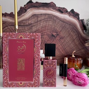 K&ouml;nnte beinhalten: Ein rosa Parf&uuml;mset mit passender Schachtel, Flasche und Probenampulle. Die Schachtel und die Flasche weisen goldfarbene Akzente und arabische Schrift auf. Das Set ist mit "Pink to Pink" und "Ajwad" beschriftet. Eine kleine Probenampulle ist mit "Lattafa" beschriftet.
