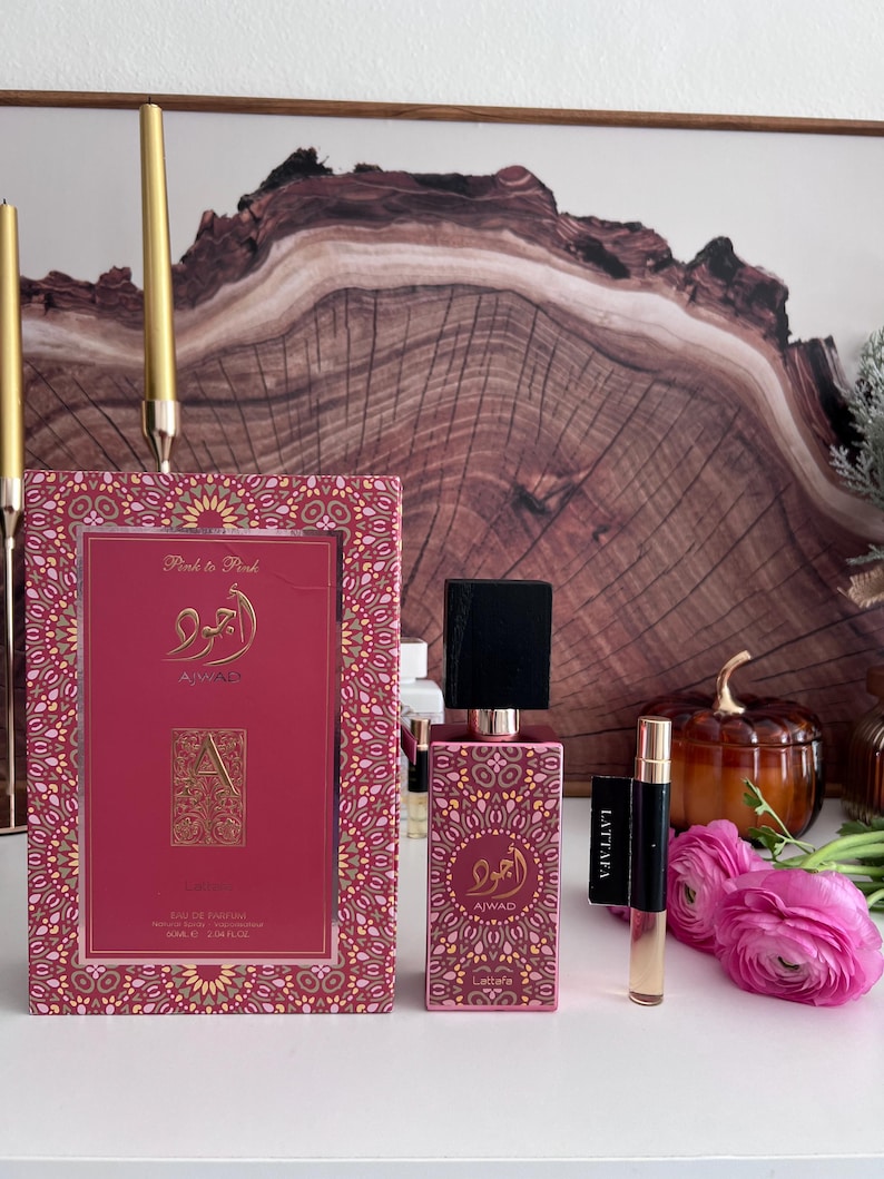 K&ouml;nnte beinhalten: Ein rosa Parf&uuml;mset mit passender Schachtel, Flasche und Probenampulle. Die Schachtel und die Flasche weisen goldfarbene Akzente und arabische Schrift auf. Das Set ist mit "Pink to Pink" und "Ajwad" beschriftet. Eine kleine Probenampulle ist mit "Lattafa" beschriftet.