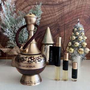 May include: A decorative hookah with a gold finish, brown accents, and floral engravings. The base reads "DREAM OF HAZE." Several small perfume bottles with black caps and labels are also present, alongside a small silver Christmas tree.