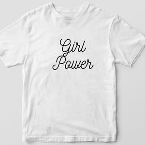 May include: White t-shirt with the words "Girl Power" in black cursive script. The shirt is made of a soft material and has short sleeves and a crew neck. The text is centered on the front of the shirt.