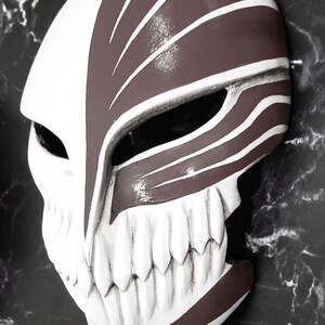 May include: A white and brown mask with a skull-like design. The mask features a prominent jawline with white teeth and a split design with brown and white stripes. The mask is likely for cosplay or costume use.