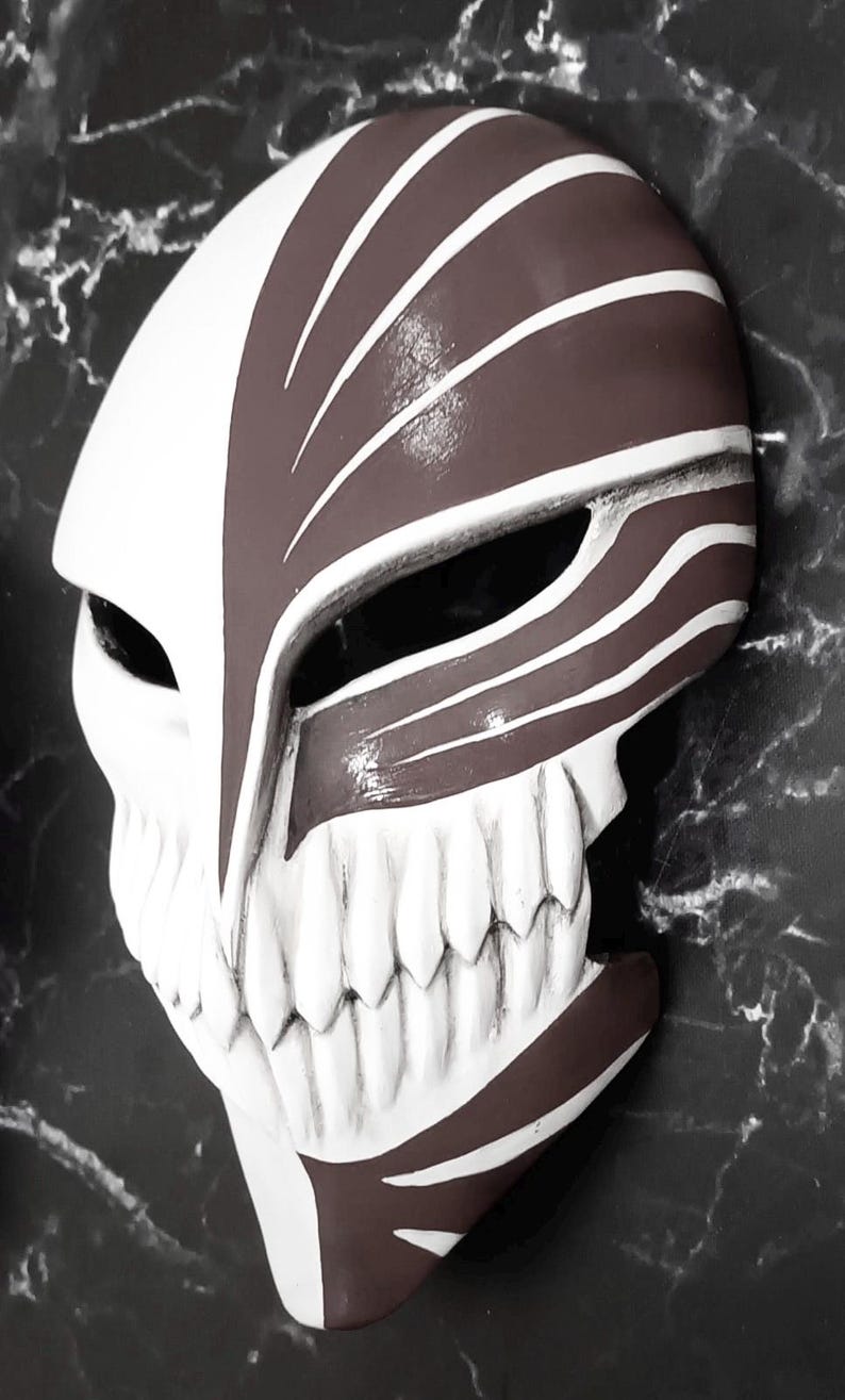 May include: A white and brown mask with a skull-like design. The mask features a prominent jawline with white teeth and a split design with brown and white stripes. The mask is likely for cosplay or costume use.