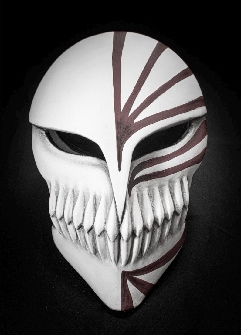 May include: A white mask with a skull-like design, featuring sharp teeth and dark red markings. The mask has a pointed chin and eye openings, with red lines radiating from the forehead. The overall aesthetic is reminiscent of a fantasy or anime theme.