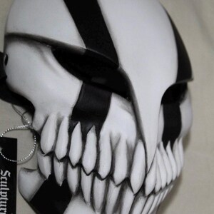 May include: A white and black mask with a skull-like design. The mask features black stripes and sharp, pointed teeth. The mask has a tag that says "Sculpture".