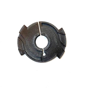 May include: A black, circular object with a split design, featuring a central hole and textured surface. The object has a unique, geometric shape, possibly a component or decorative item.