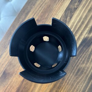 May include: Black plastic cup with six holes around the rim. The cup is designed to hold multiple items, such as pens or pencils.